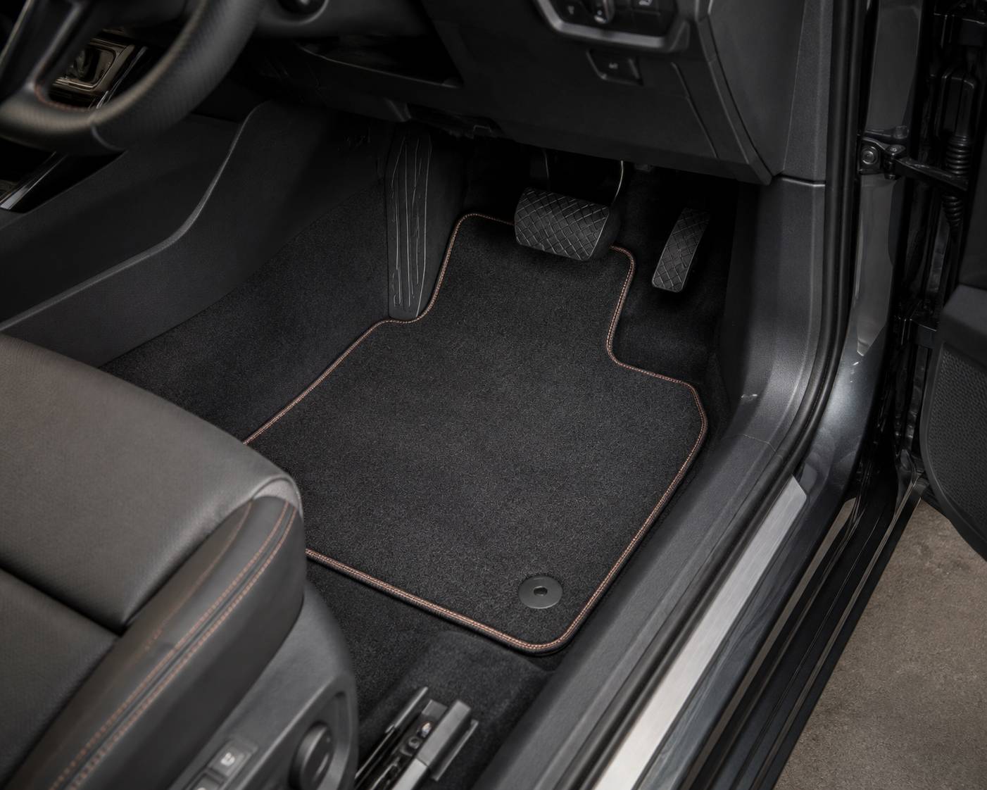 Tailored charcoal car mat with a bound edge, fitted in a vehicle footwell over the original fixing point